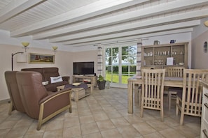 A spacious living room with a sofa, TV, and dining area. - Beachfront idyll by the sea, private bathing area - Gutshof Ostseeblick FeWo 01 - (Putbus)