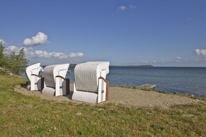 Wicker chairs on a sandy beach with a view of the sea and a distant island. - Idyllic seaside location close to the beach, private bathing area - Gutshof Ostseeblick FeWo 03 - (Putbus)