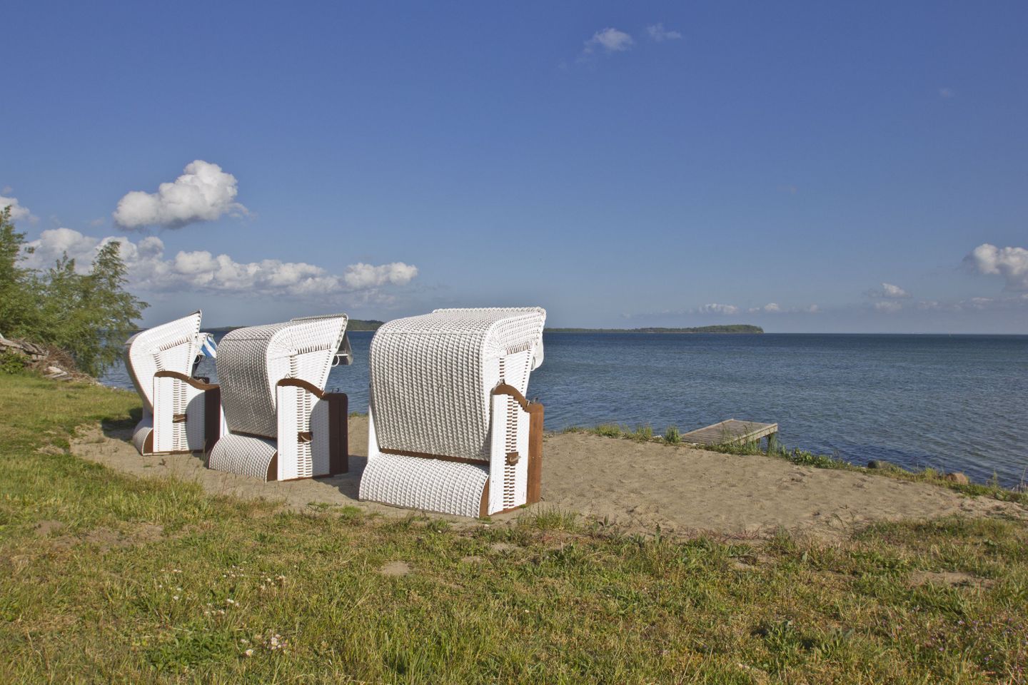 Wicker chairs on a sandy beach with a view of the sea and a distant island.