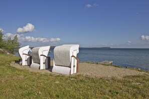 Des chaises en osier sur une plage de sable, avec vue sur la mer et une île lointaine.
