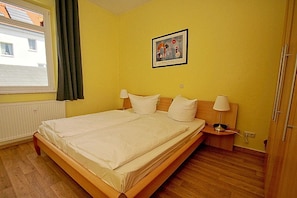A double bed in a room with yellow walls, a window with curtains, a framed picture on the wall, and a bedside table with a lamp. - Quiet location, vacation apartment in seaside style with veranda - Villa Möwe FeWo 06 - Villa (Göhren)