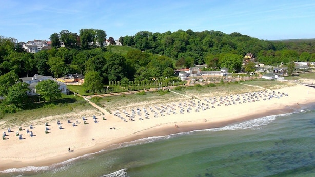 Une plage parsemée de nombreux parasols et de chaises longues, une étendue de sable et, en arrière-plan, une colline boisée.