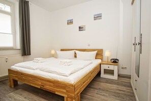 A neatly made bed with white linens and pillows, a wooden headboard, a bedside table with a lamp, and a small bedside radio. - Quiet location, porch, free use of the AHOI adventure pool - Villa Möwe FeWo 01 - (Göhren)