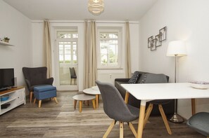 Ein modernes Wohnzimmer mit Fernseher, einer Couch, einem Esstisch und Stühlen.