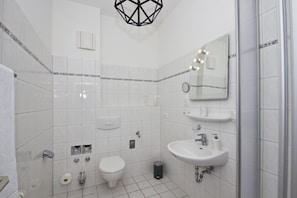 A modern bathroom with white tiles, a toilet, a sink, and a shower area. - Quiet location, seaside-style vacation apartment with conservatory - Villa Möwe FeWo 04 - (Göhren)