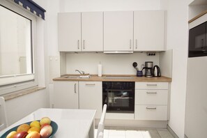 A compact kitchen with white cabinets, a wooden countertop, a built-in oven, and a window.