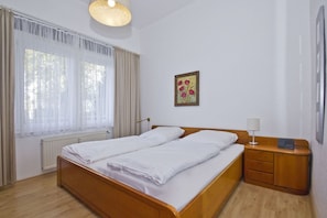 A double bed with white linens, a bedside table with a lamp, a framed picture on the wall, and a window with sheer curtains. - Quiet location with a terrace; access to the pool and sauna - Villa Käthe FeWo 04 - (Göhren)