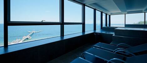 A room with large windows, a view of the sea, and a pier.