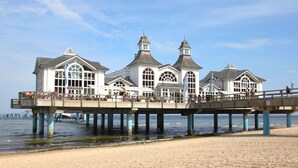 A pier with a white building featuring arched windows and a central tower, extending over the beach. - Pool and sauna with sea view, directly at the pier - FIRST Sellin FeWo 2.3 - (Sellin)