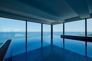 Une piscine à débordement moderne offrant une vue dégagée sur l’océan et une jetée visible au loin.