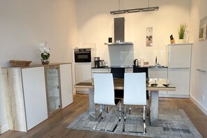 A modern kitchen with a dining area, featuring a central island, white cabinetry, and a built-in oven. - Pool and sauna with a view of the sea, right on the pier - FIRST Sellin FeWo 2.3 - (Sellin)