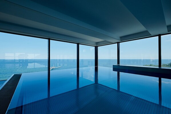 A modern infinity pool with a clear view of the ocean and a pier in the distance.
