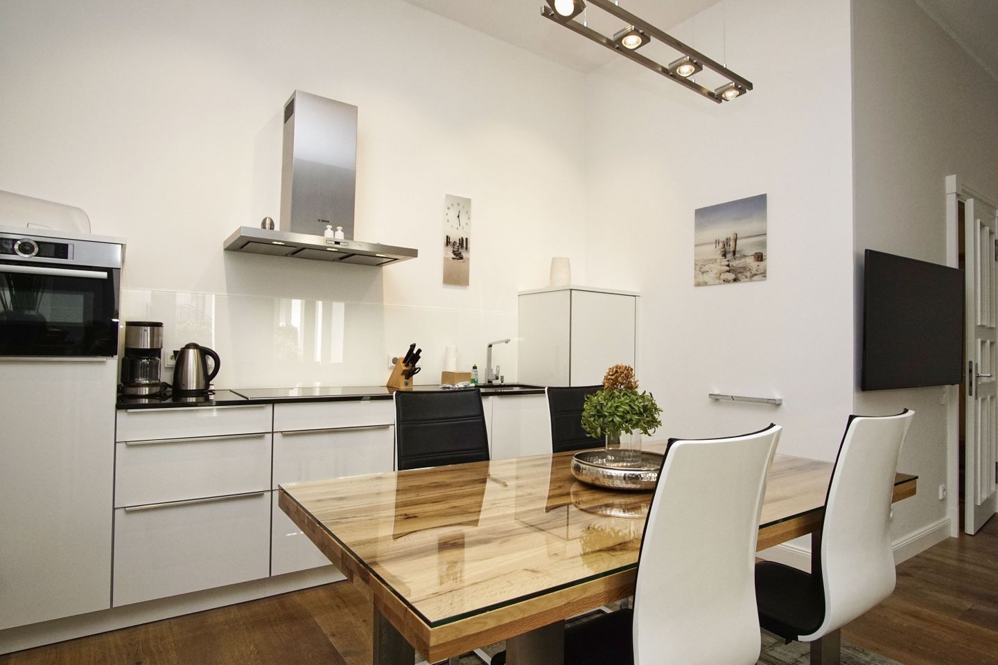 Een moderne keuken met witte kasten, een roestvrijstalen afzuigkap, een koffiezetapparaat en een eettafel met stoelen.