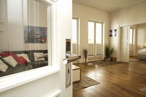 A spacious living area with a wooden floor, a sofa with cushions, a dining table, and a potted plant.