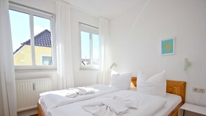 Une chambre d’hôtel propre et bien éclairée, avec deux lits, du linge de lit blanc et une vue sur un bâtiment à l’extérieur.