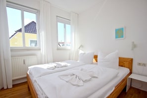 Une chambre d’hôtel propre et bien éclairée, avec deux lits, du linge de lit blanc et une vue sur un bâtiment à l’extérieur.