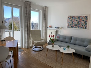 Un salon avec un canapé gris, un fauteuil blanc, une table à manger avec des chaises et une petite table basse.