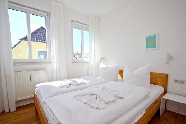 A clean, well-lit hotel room with two beds, white linens, and a view of a building outside.
