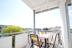 Un balcon avec une table et des chaises, une vue sur le quartier et une balustrade blanche.