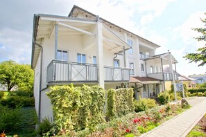 Ein mehrstöckiges Gebäude mit Balkonen, einer Veranda und einem Garten mit Blumen und Sträuchern.