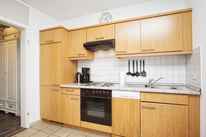 A kitchen with wooden cabinets, a stove, a dishwasher, and a clock on the wall. - Die Ferienwohnung Nr. 27 in der Villa Buskam - Villa Buskam (Göhren)