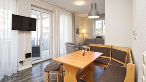 Una sala de estar moderna con una mesa de madera, dos sillas, un sofá, un televisor montado en la pared y una lámpara de techo.