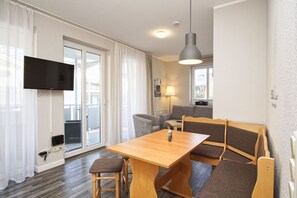 A modern living room with a wooden table, two chairs, a sofa, a TV mounted on the wall, and a ceiling light.