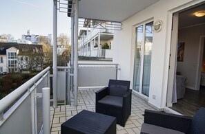 A balcony with wicker furniture, a view of neighboring buildings, and a glass door leading inside.
