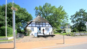 Un edificio tradicional con techo de paja y fachada blanca, un pequeño porche y una bicicleta estacionada afuera.