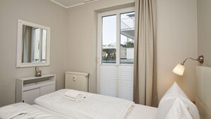 Habitación de hotel con cama, mesita de noche, espejo, ventana con cortinas y radiador.