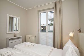 Ein Hotelzimmer mit einem Bett, einem Nachttisch, einem Spiegel, einem Fenster mit Vorhängen und einer Heizung.