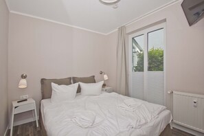 A hotel room with a bed, two bedside tables, a lamp, a TV, and a window with blinds.