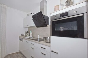 A modern kitchen with white cabinetry, a stainless steel oven, and a built-in microwave. - Die Ferienwohnung Nr. 22 in der Villa Buskam - Villa Buskam (Göhren)