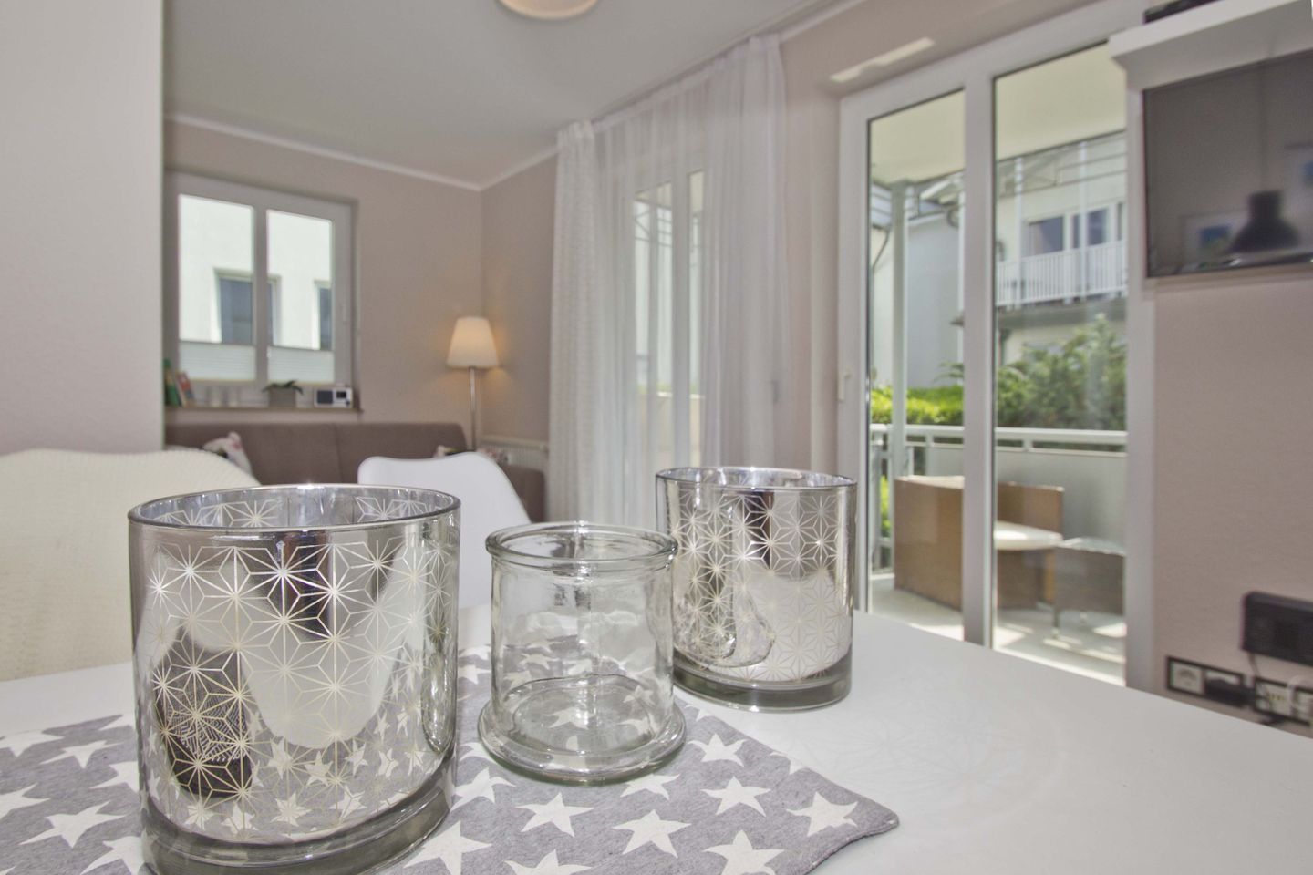 Une chambre d’hôtel avec un lit, une table sur laquelle sont posés trois photophores en verre, un balcon avec une table et des chaises, et une vue sur la verdure environnante.