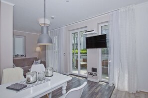 Ein modernes Wohnzimmer mit einem weißen Sofa, einem Esstisch mit Glasplatte und einem großen an der Wand befestigten Fernseher.