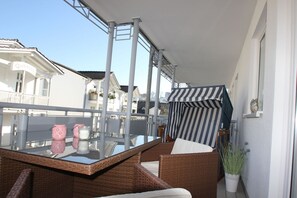 Un balcon agrémenté de meubles en osier, d’une table en verre et d’un auvent à rayures.