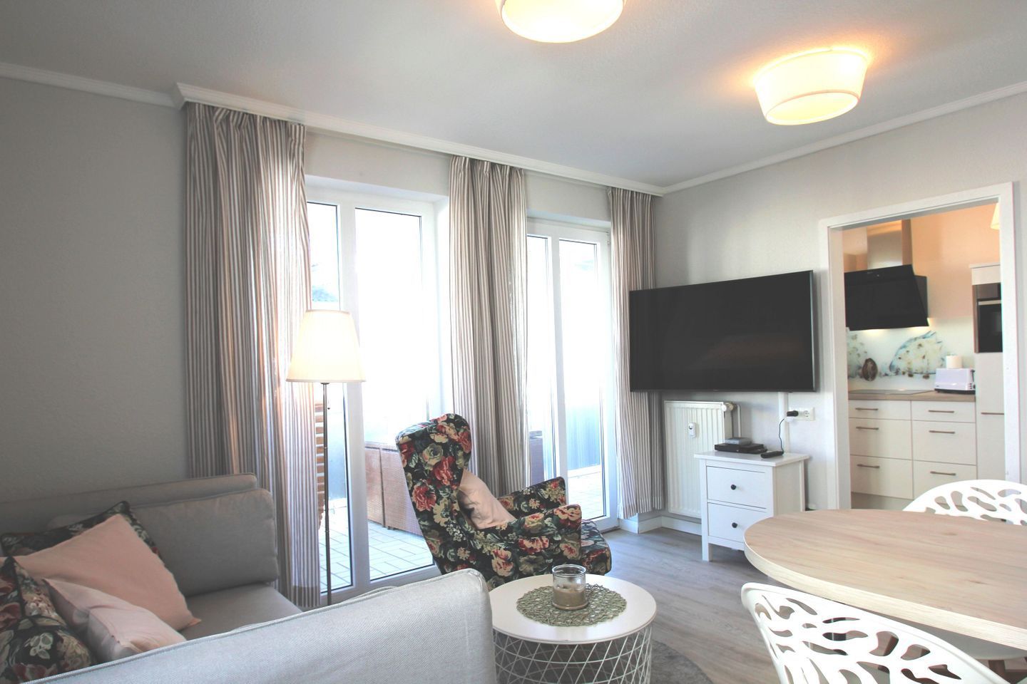 Un salon moderne comprenant un canapé, un fauteuil à motifs floraux, une table à manger et un téléviseur fixé au mur.