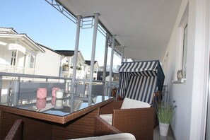 Ein Balkon mit Korbmöbeln, einem Glastisch und einem gestreiften Markisenvorzelt.