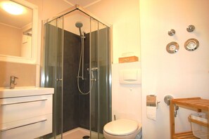 Une salle de bain moderne avec une douche à parois de verre, des toilettes blanches et un meuble-lavabo en bois avec un miroir.
