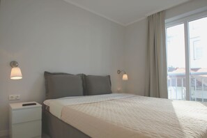 Une chambre d’hôtel avec un lit, des lampes de chevet, une table de nuit et une fenêtre donnant sur des immeubles.