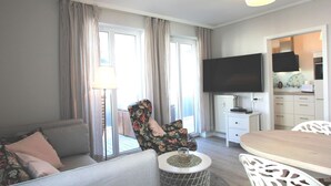 Una sala moderna con un sofá, un sillón estampado, una mesa de comedor y un televisor montado en la pared.