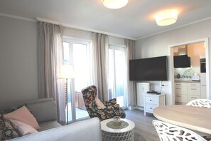 Ein modernes Wohnzimmer mit einer Couch, einem floralen Sessel, einem Esstisch und einem an der Wand montierten Fernseher.