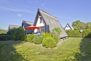 Une maison avec un toit à forte pente, entourée de haies bien entretenues et d’une pelouse.