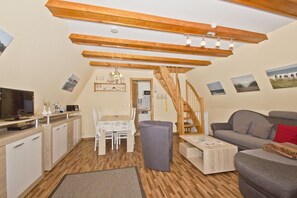 Een knus loft-achtig woongedeelte met een keuken, een eethoek en een trap naar een hoger gelegen niveau.