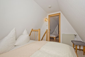 A small, cozy attic bedroom with a sloped ceiling, a wooden bed frame, a single bedside chair, and a radiator.