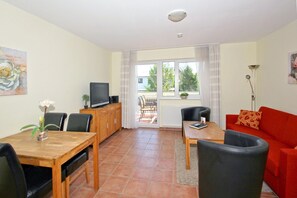 Ein Wohnzimmer mit Essbereich, einem roten Sofa, einem Fernseher und Blick ins Freie.