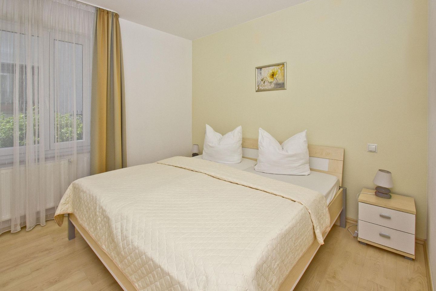 A hotel room with a bed, a nightstand, a lamp, and a window with curtains.