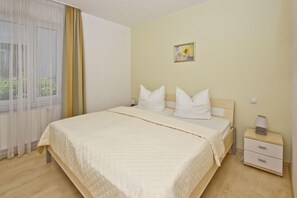Quarto de hotel com cama, mesa de cabeceira, luminária e janela com cortinas.