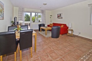 A living room with a dining area, a red sofa, and a coffee table. - Central but quiet, balcony, free swimming pool and sauna - Villa Elisenhof apartment 2 (Göhren)