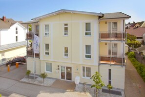 A multi-story hotel with a light yellow facade, balconies on the upper floors, and a small entrance area with a sign. - Central but quiet, balcony, free swimming pool and sauna - Villa Elisenhof apartment 2 (Göhren)